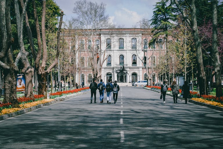 Students walking on a university campus surrounded by trees and spring flowers.